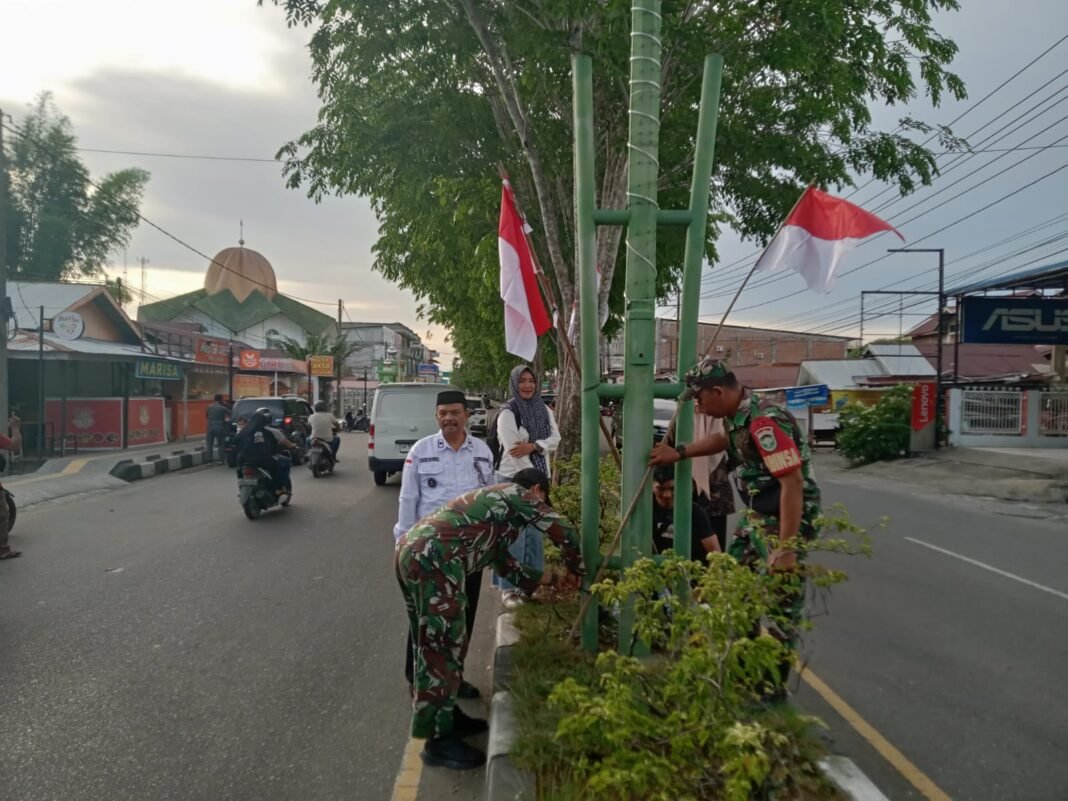 Babinsa Koramil 07/Johan pahlawan bantu kepala desa dan aparatur desa Drin Rampak memasang bendera merah putih di sepanjang jalan protokol
